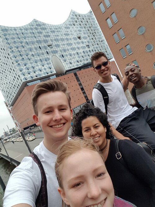 Fünf junge Freiwilligendienstleistende, welche vor der Elbphilharmonie ein Selfie machen. Alls lächeln.